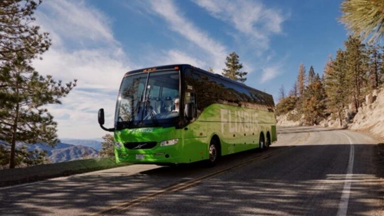 A bus travels on a highway with trees and rocks in the background.