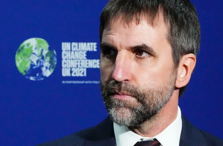 A bearded man stands in front of a sign that says UN Climate Change Conference UK 2021