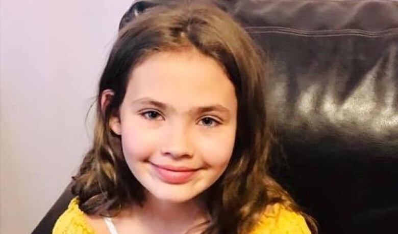 girl with long brown hair wears a yellow t-shirt