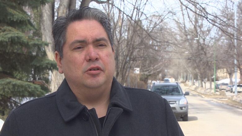 A man with gray-black hair stands outside