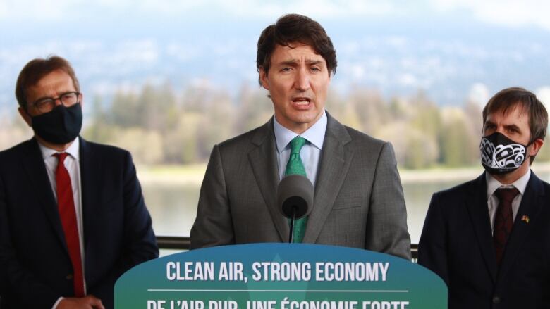 Three men, two of them masked, stand behind a podium.