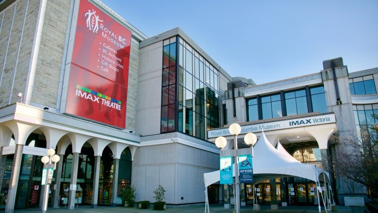 The exterior of the Royal B.C. Museum with exterior globed lighting, a pavillioned entrance and signs advertising an IMAX experience.