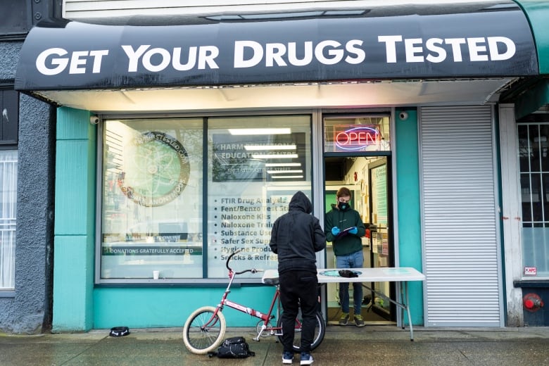 A man stands at the door under an awning that says 