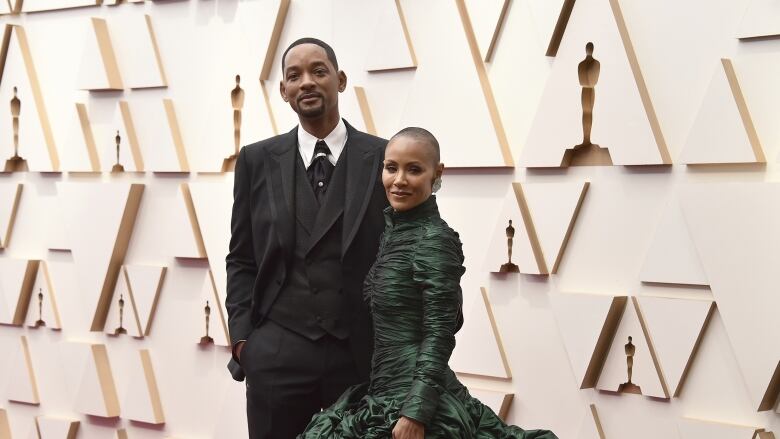 A couple dressed in formalwear attend a red carpet event.