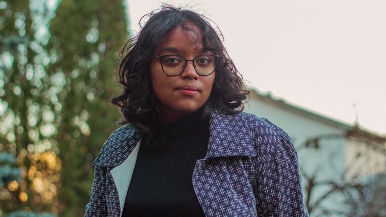 A woman with dark hair wearing glasses and a blue patterned jacket over a black turtleneck sweater