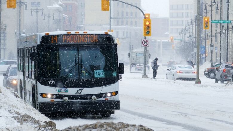 A bus is driving through an intersection during a snow storm. A street sign says 