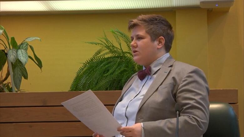 A woman stands holding a piece of paper in a government legislature.