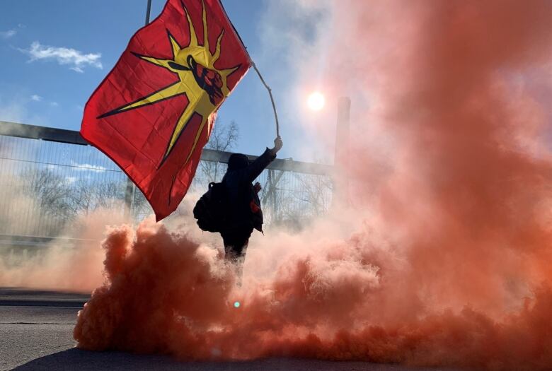 A person holds up a red flag and stands among red smoke.