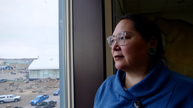 A woman stands inside, looking out a window.