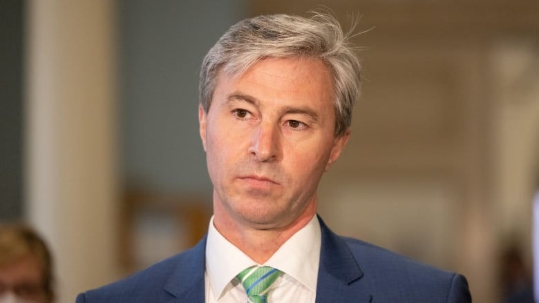 A grey-haired man in a suit and ties stares pensively.