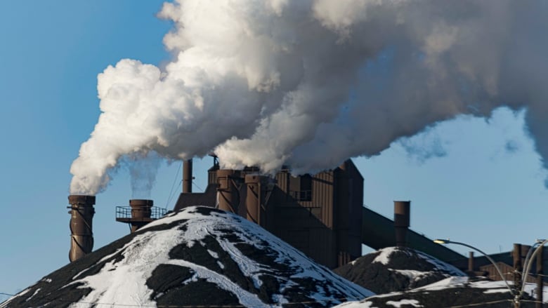 Smoke stacks release plumes of white smoke into the air from a factory. 