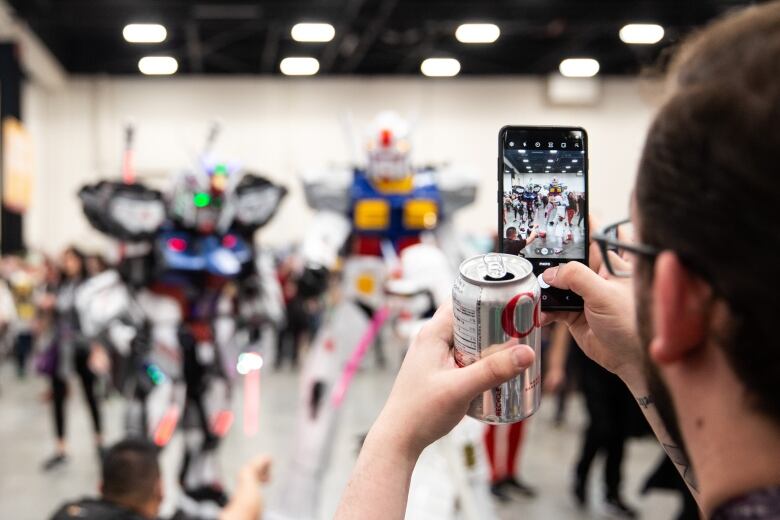 A fan snaps a photo of two cosplayers dressed as Gundams  at the Calgary Comic and Entertainment Expo Stampede Park in Calgary, AB on April 23, 2022. 