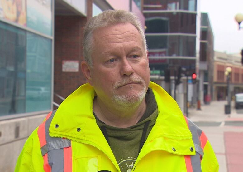 A man wearing a yellow reflective jacket stands on a street in downtown St. John's.