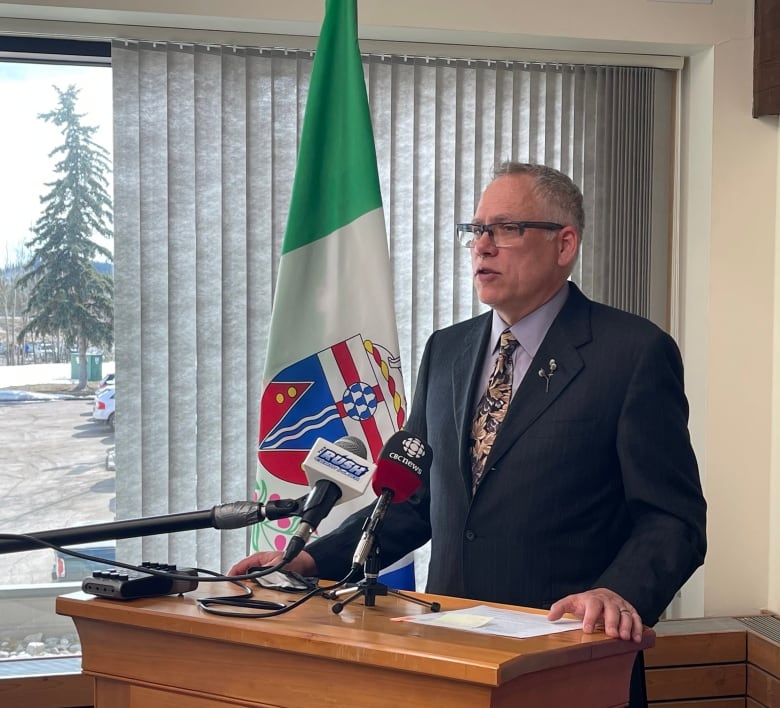 Man in suit speaks into microphones at a podium.