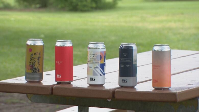 five beer cans in a row on a picnic table