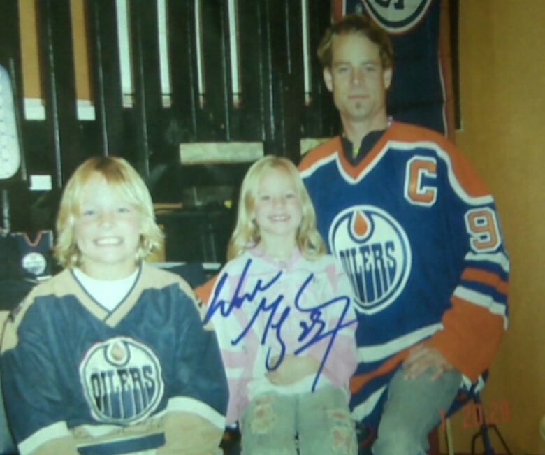 A photo signed by Wayne Gretzky of a young man in a blue and orange Edmonton Oilers hockey jersey sitting next to two children also wearing jerseys. 