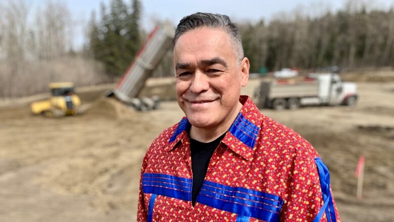 Man in traditional Cree shirt smiles at camera on the site under construction.