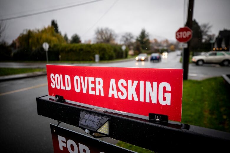 A red 'sold over asking' sign is pictured on a rainy day.