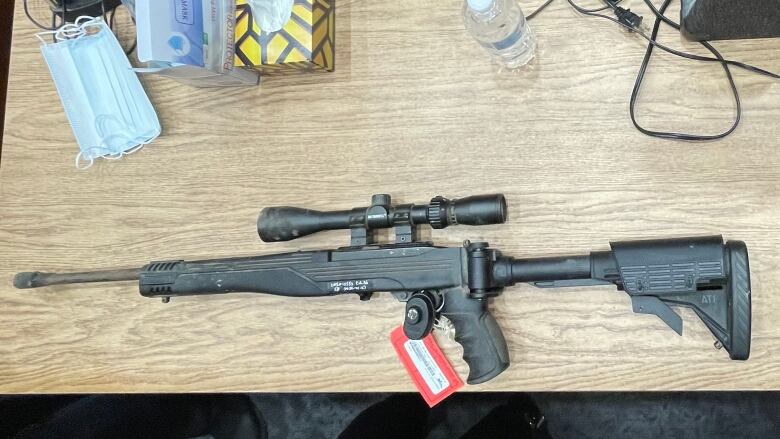 A rifle with a scope is shown on a table in the courtroom. 