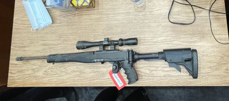 A rifle with a scope is shown on a table in the courtroom. 