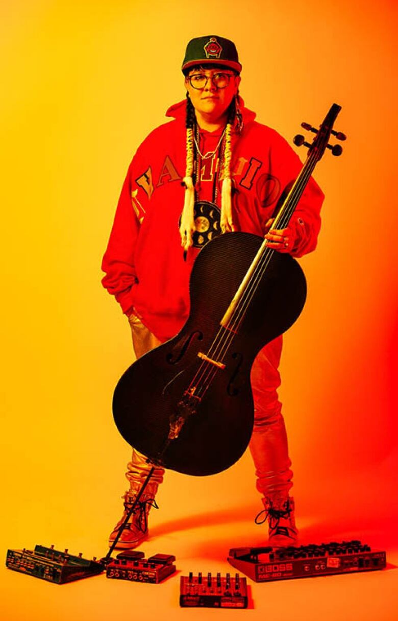 An Indigenous women with hair ties hold a black cello 