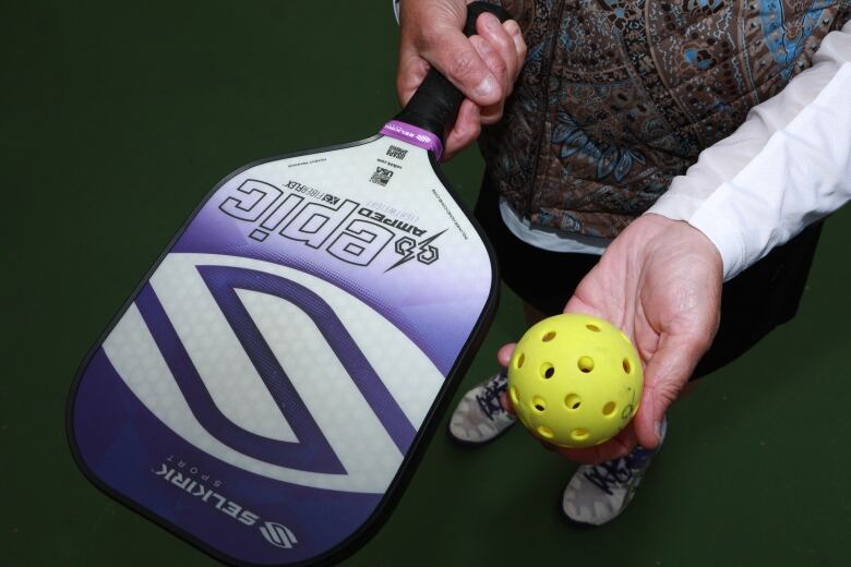 A woman holds a pickleball paddle and ball in this close-cropped photo.