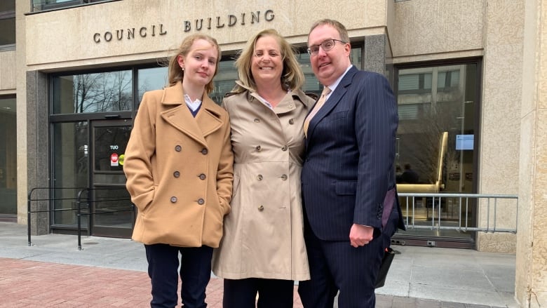 Three people in fall clothing, standing outside a building.