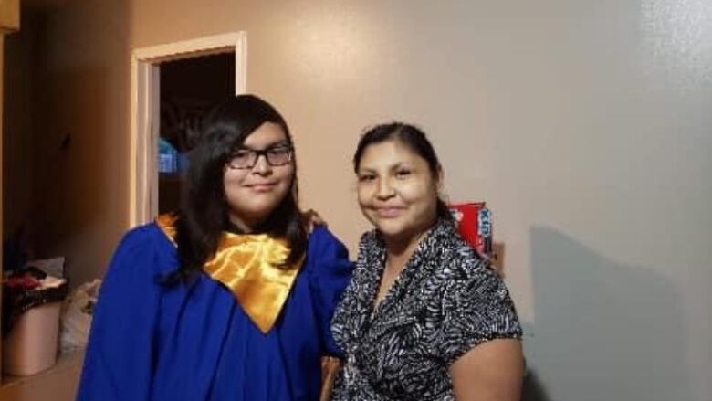 A person in a blue graduation gown stands beside a woman. They are both smiling.