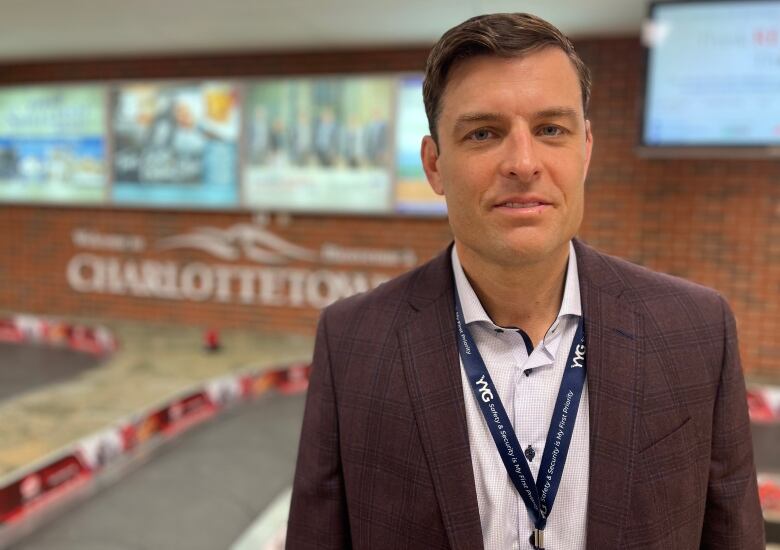 A man with short dark hair wearing a dark blazer over a white shirt and standing inside an airport lobby.