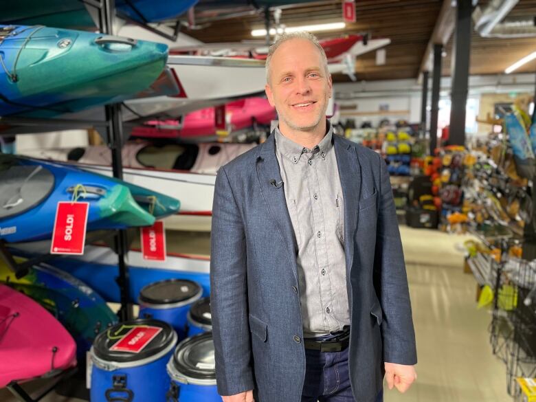 A man in a dark bluish blazer and grey button-up shirt stands in a wilderness supply store.