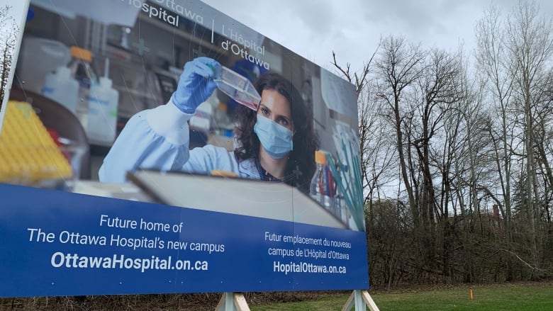 A billboard in front of trees shows a hospital setting with an employee wearing a mask.