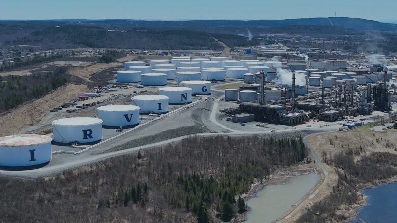 An overhead shot of an oil refinery, with a variety of storage tanks. Six in a row in the foreground are white with letters spelling out 