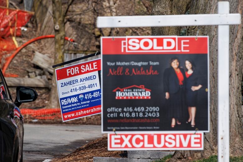 Two real estate signs are in front of each other, one says sold the other says for sale.