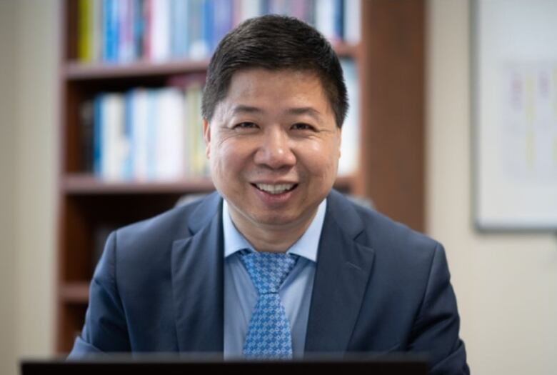 A person with black hair wearing a suit and tie smiles.