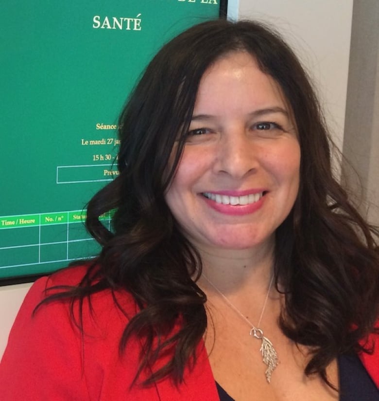 A woman with dark hair wearing a red blazer, smiles. 