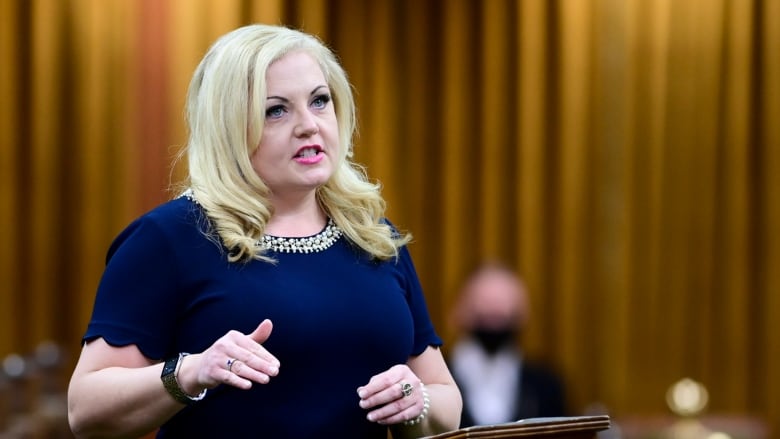 A woman in a blue dress motions with her hands as she speaks in the House of Commons.