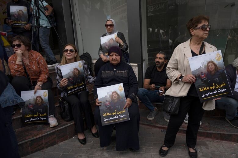 Women hold photos of a slain journalist on a sidewalk.