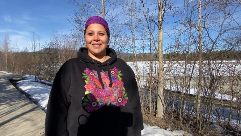 A smiling woman stands beside an ice-covered river on a sunny day.