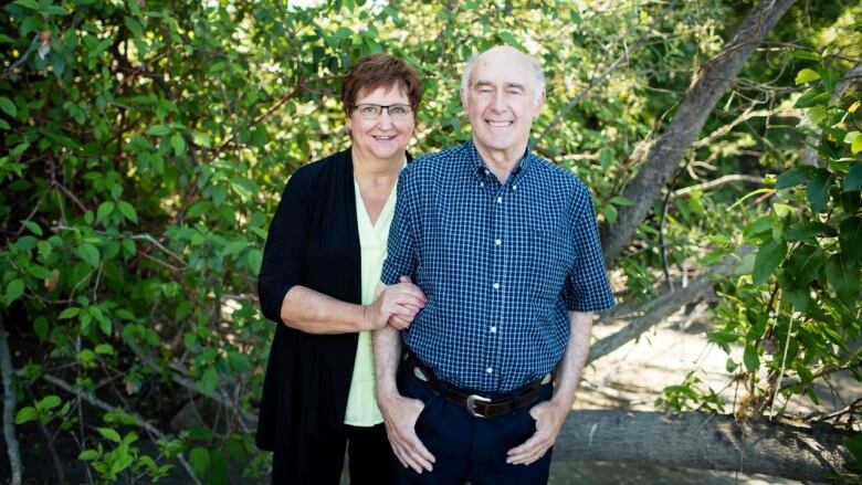 A woman with short brown hair holds the hand of a man with white hair.