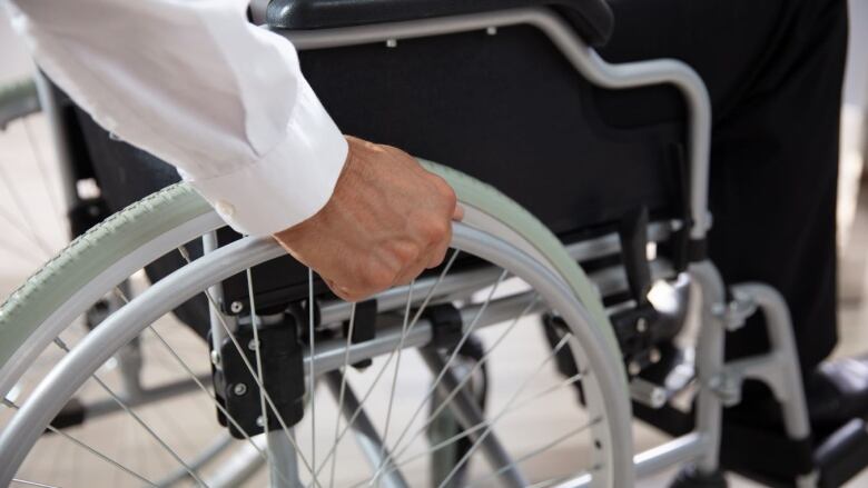 Someone sits in a wheelchair and their hand rests on one of the wheels.