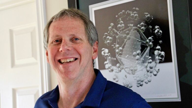 A portrait of a smiling man with short grey hair, wearing a blue collared shirt.