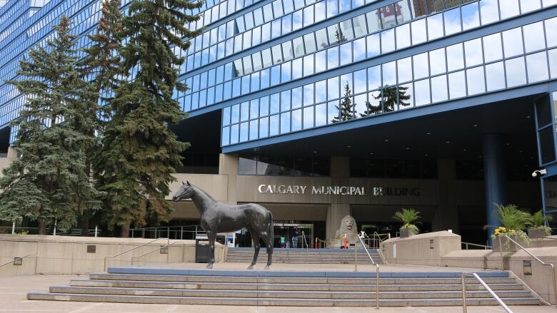 A building with many glass windows. There is a statue of a horse in front of the building. 