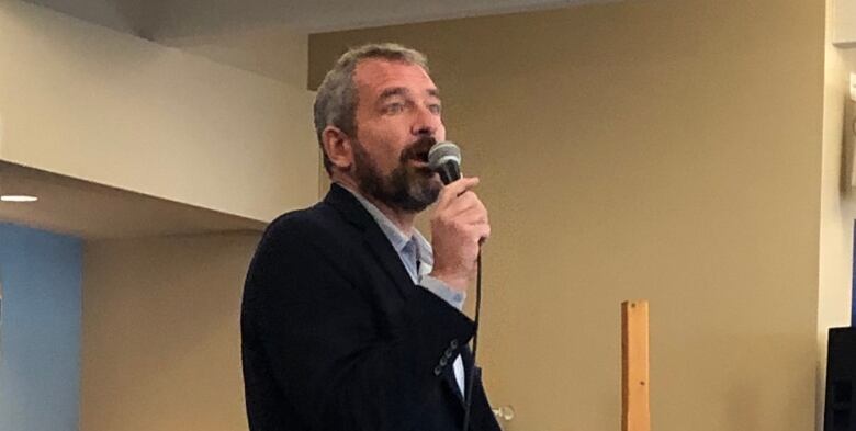 Man speaking at a meeting with a microphone in his hand.