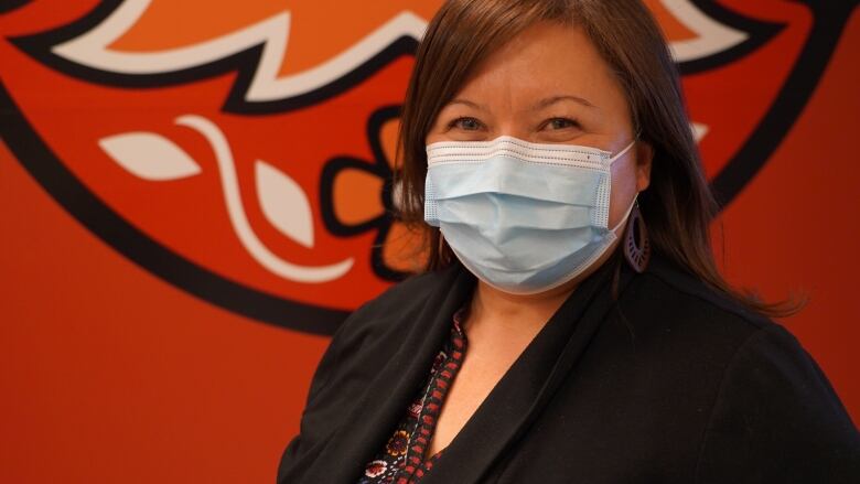 A woman wearing a mask smiles for a picture.