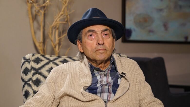 An elderly Indigenous man wearing a black hat is pictured looking toward the camera.