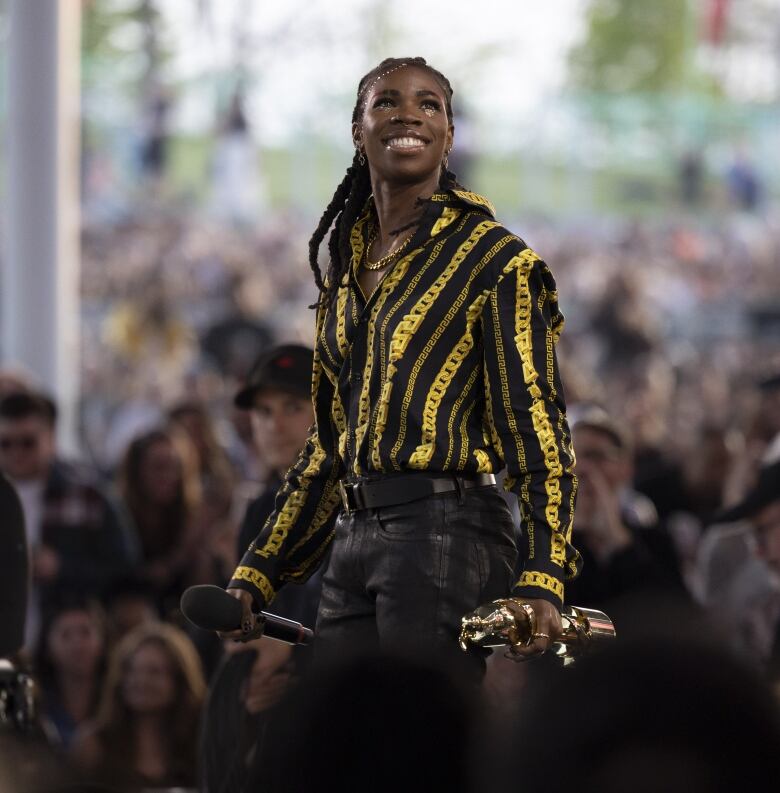 A person with big gold chains and a cool dress shirt looks awesome and holds a Juno award.