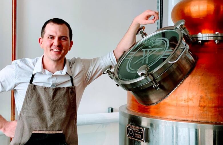 A man stands next to brewing equipment.