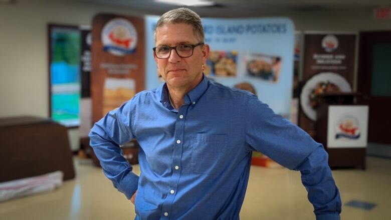 A man in a blue shirt stands in front of a banner showing potatoes 