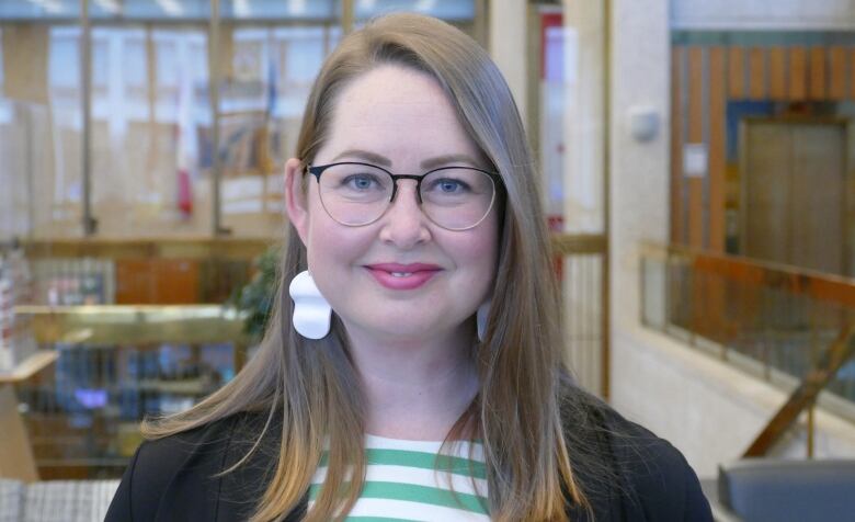 A woman with long hair, glasses and a striped t-shirt underneath a black cardigan.