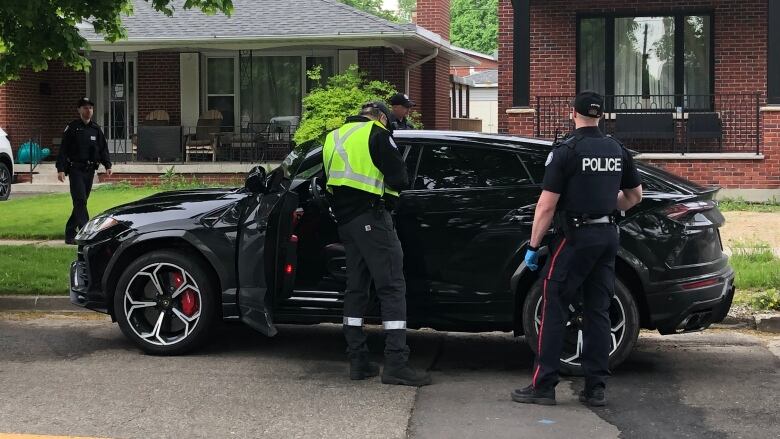 Man in yellow vest makes notes beside a car parked on a street with its door open.